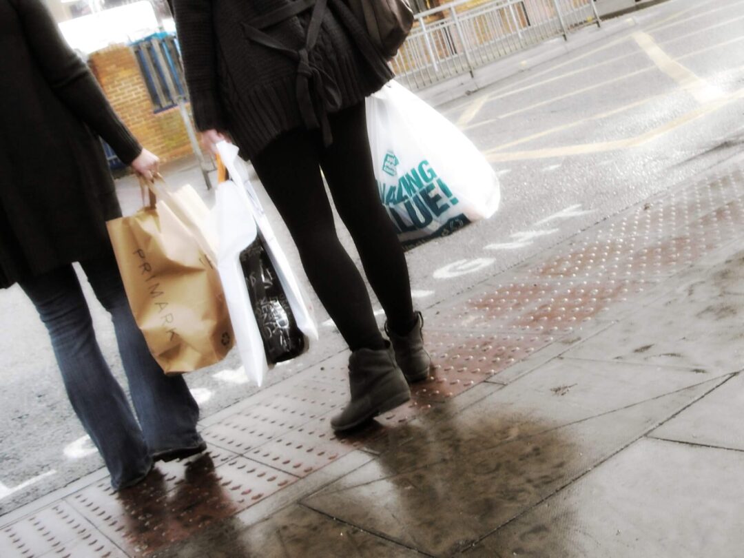 Zwei Frauen mit Einkaufstüten an einer Straße, unter anderem sind die Taschen von der Modekette Primark