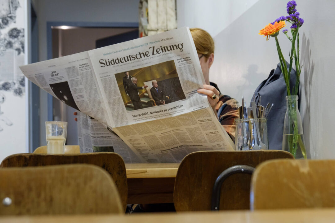 Eine Frau sitzt im Cafe und liest gemütlich eine gedruckte Ausgabe der Süddeutschen Zeitung