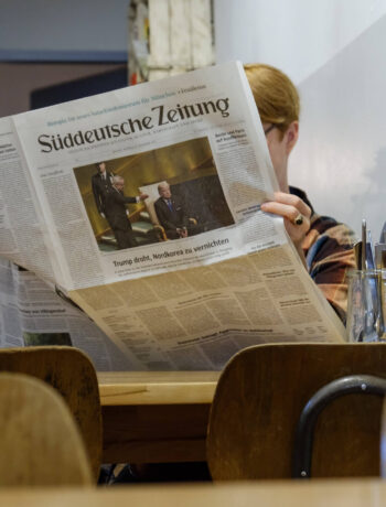 Eine Frau sitzt im Cafe und liest gemütlich eine gedruckte Ausgabe der Süddeutschen Zeitung
