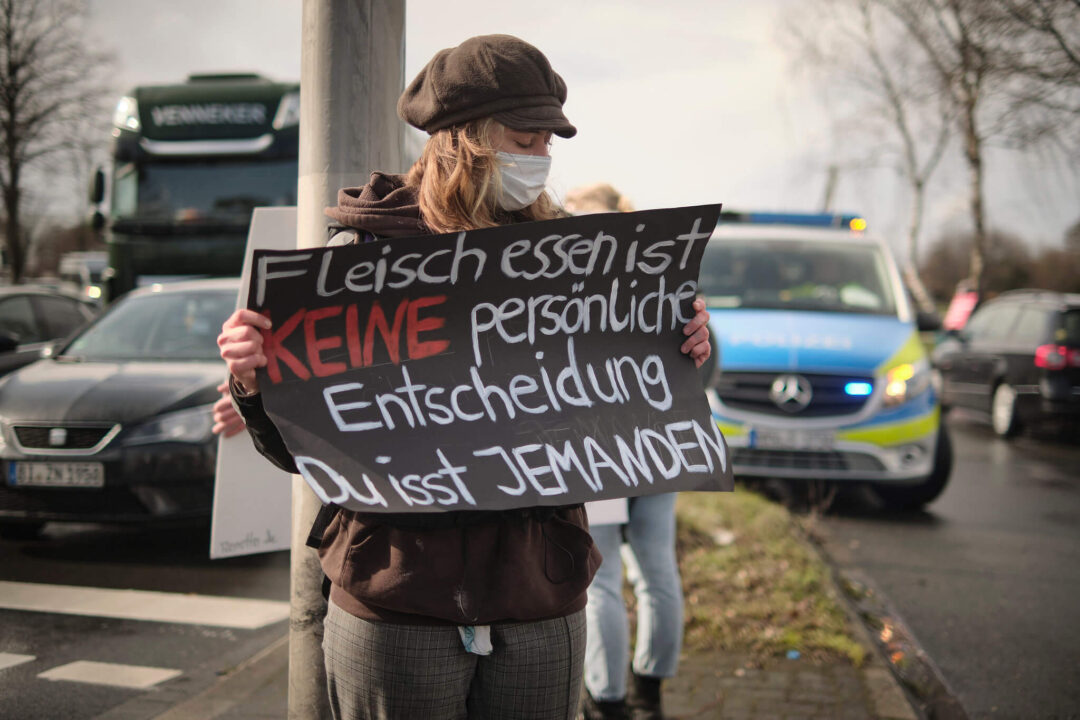 Vegane Aktivistin zeigt ein Protestschild und macht vor Fleischfabrik auf Tierleid aufmerksam