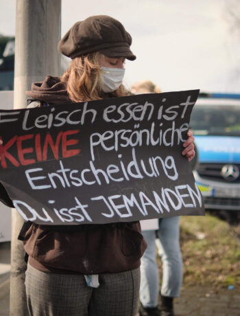Vegane Aktivistin zeigt ein Protestschild und macht vor Fleischfabrik auf Tierleid aufmerksam