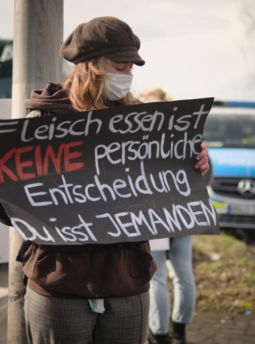 Vegane Aktivistin zeigt ein Protestschild und macht vor Fleischfabrik auf Tierleid aufmerksam